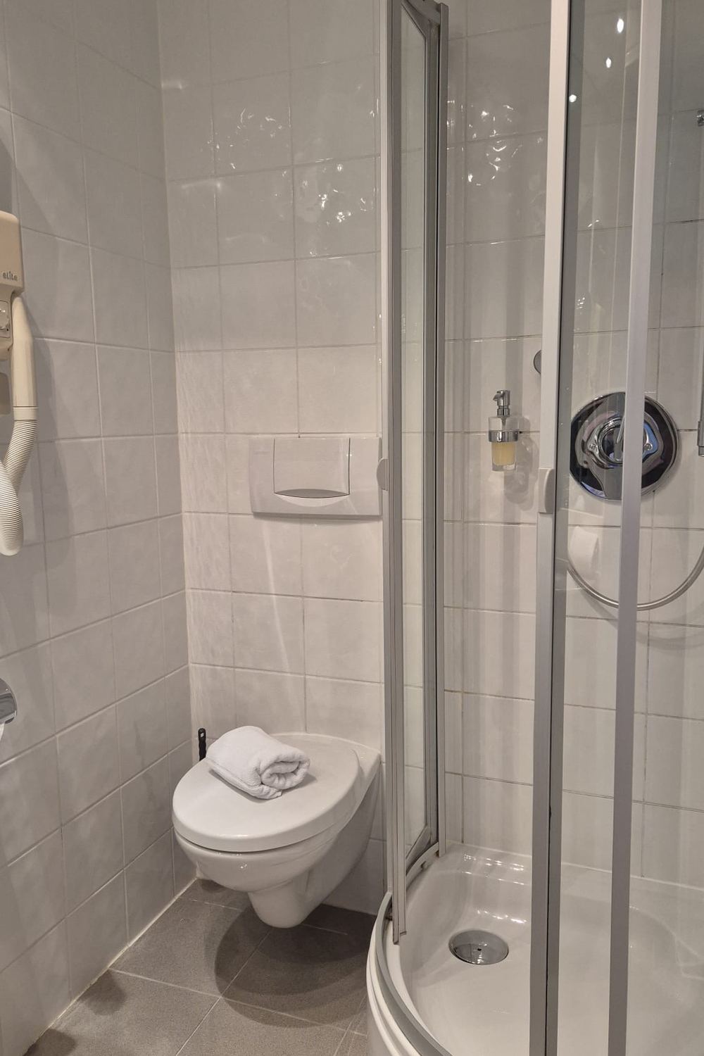 WC und Duschkabine, an der Wand ein Föhn